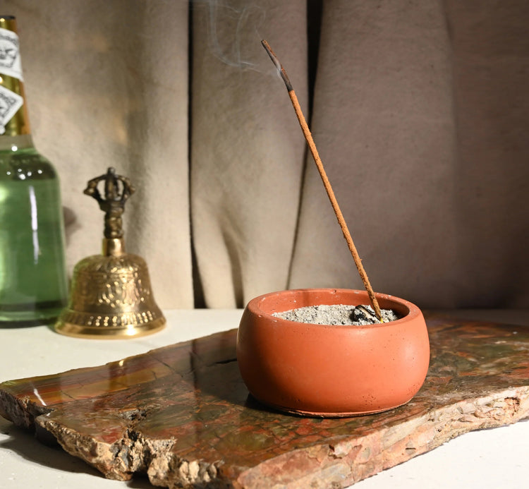 Burning stick incense on stoneware with bell in the background.
