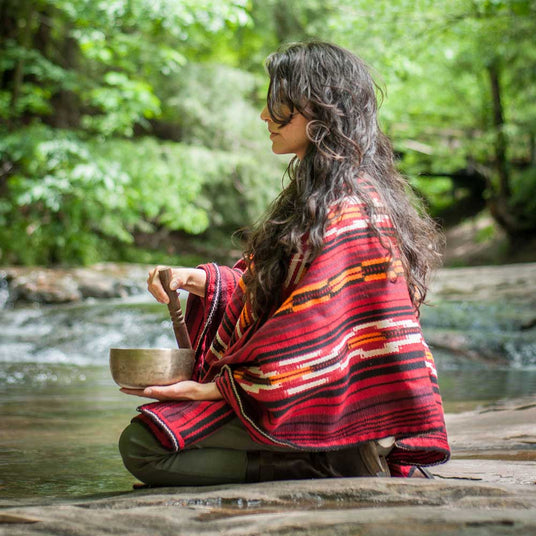 Woman wearing a red Peruvian poncho meditating using a hand-made signing bowl.